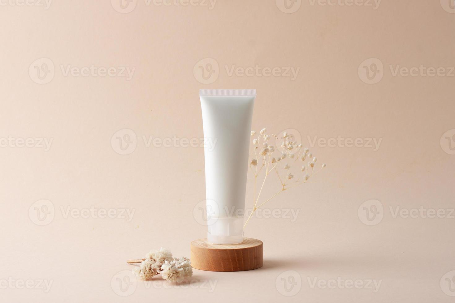 tubo branco de creme cosmético com flores no pódio de madeira sobre fundo bege. fechar-se. foto