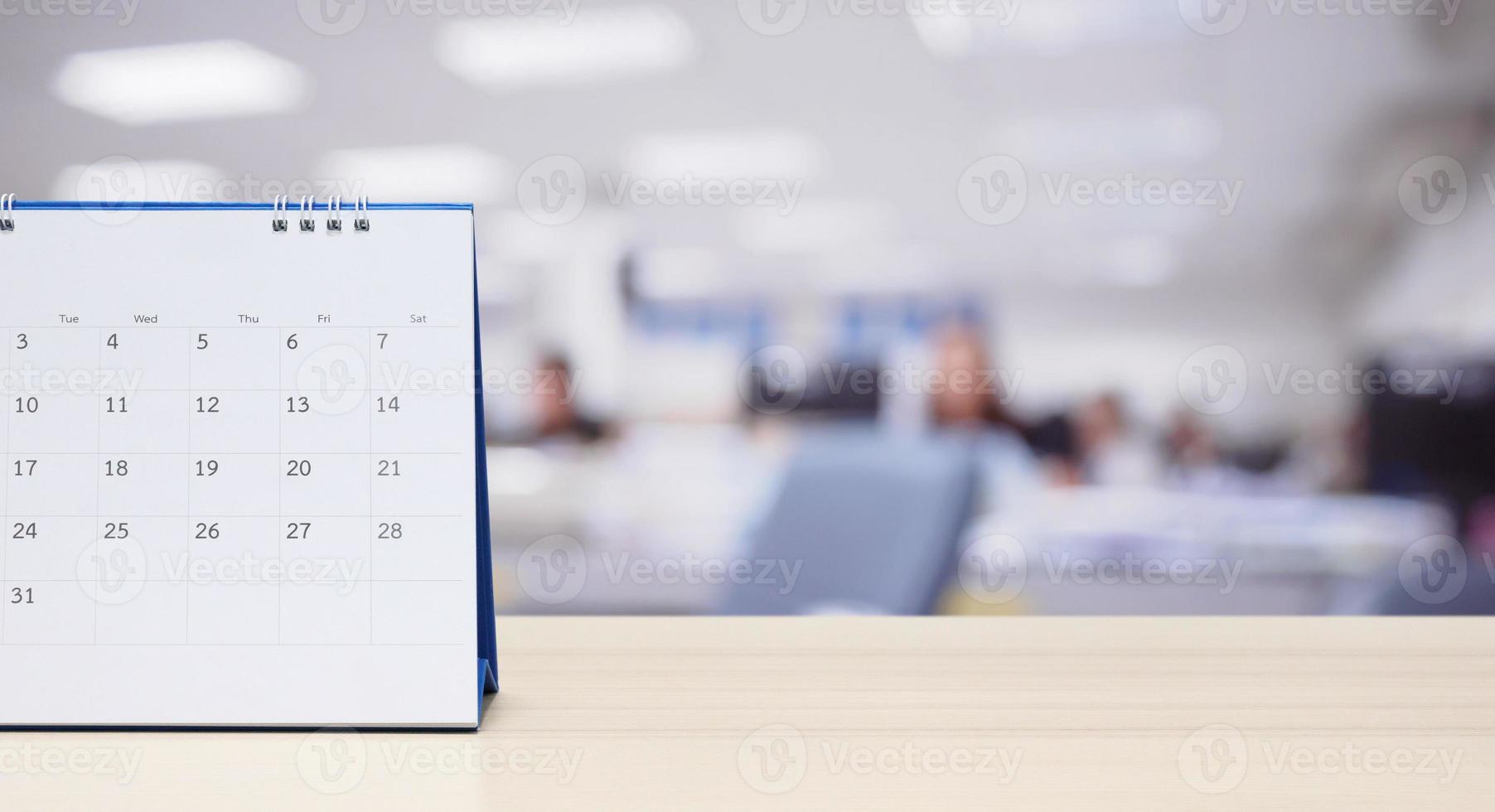 calendário de mesa de papel branco no tampo da mesa de madeira com fundo interior de escritório turva foto