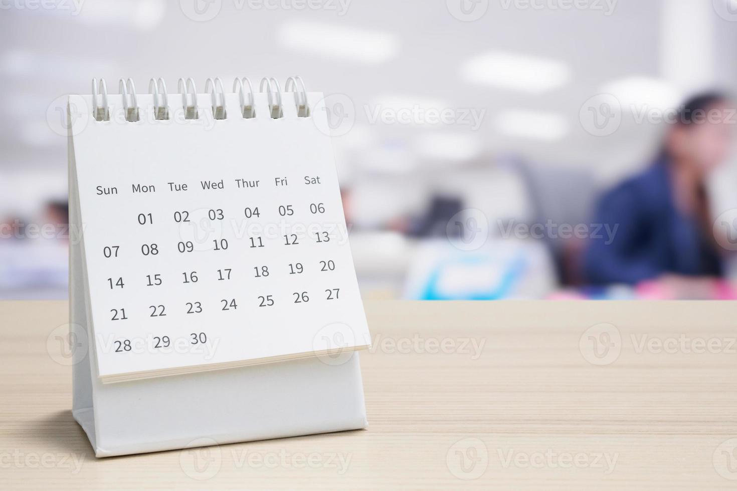 calendário de mesa de papel branco no tampo da mesa de madeira com fundo interior de escritório turva foto