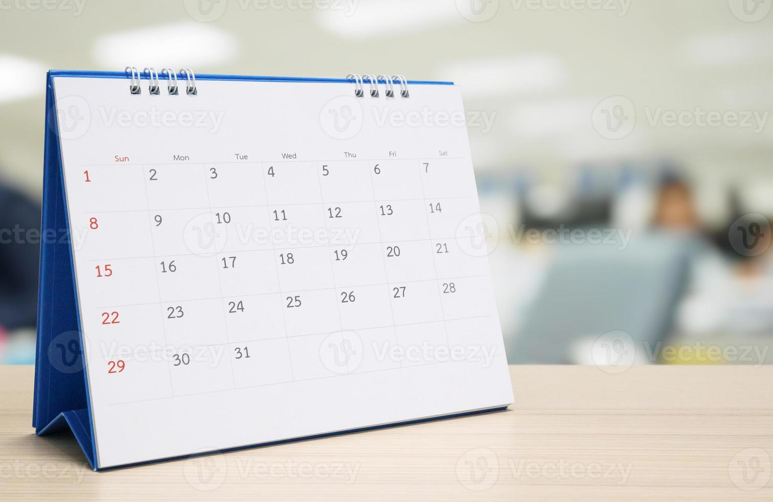 calendário de mesa de papel branco no tampo da mesa de madeira com fundo interior de escritório turva foto