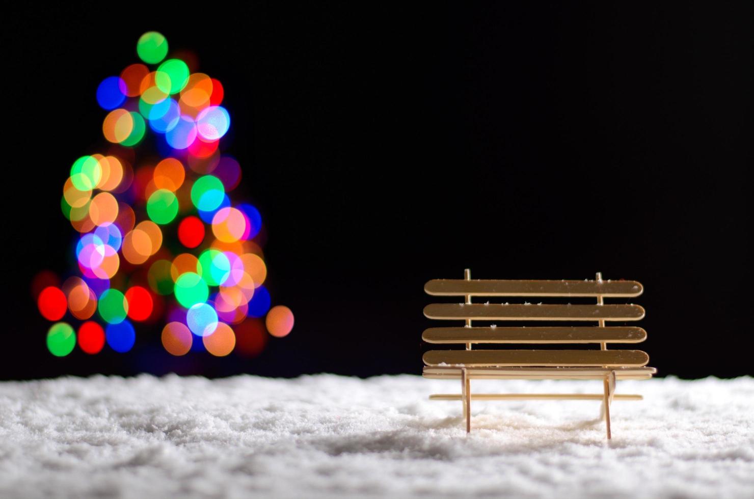 banco de madeira ao nevar no chão na temporada de inverno e luzes coloridas de bokeh da árvore de natal. foto