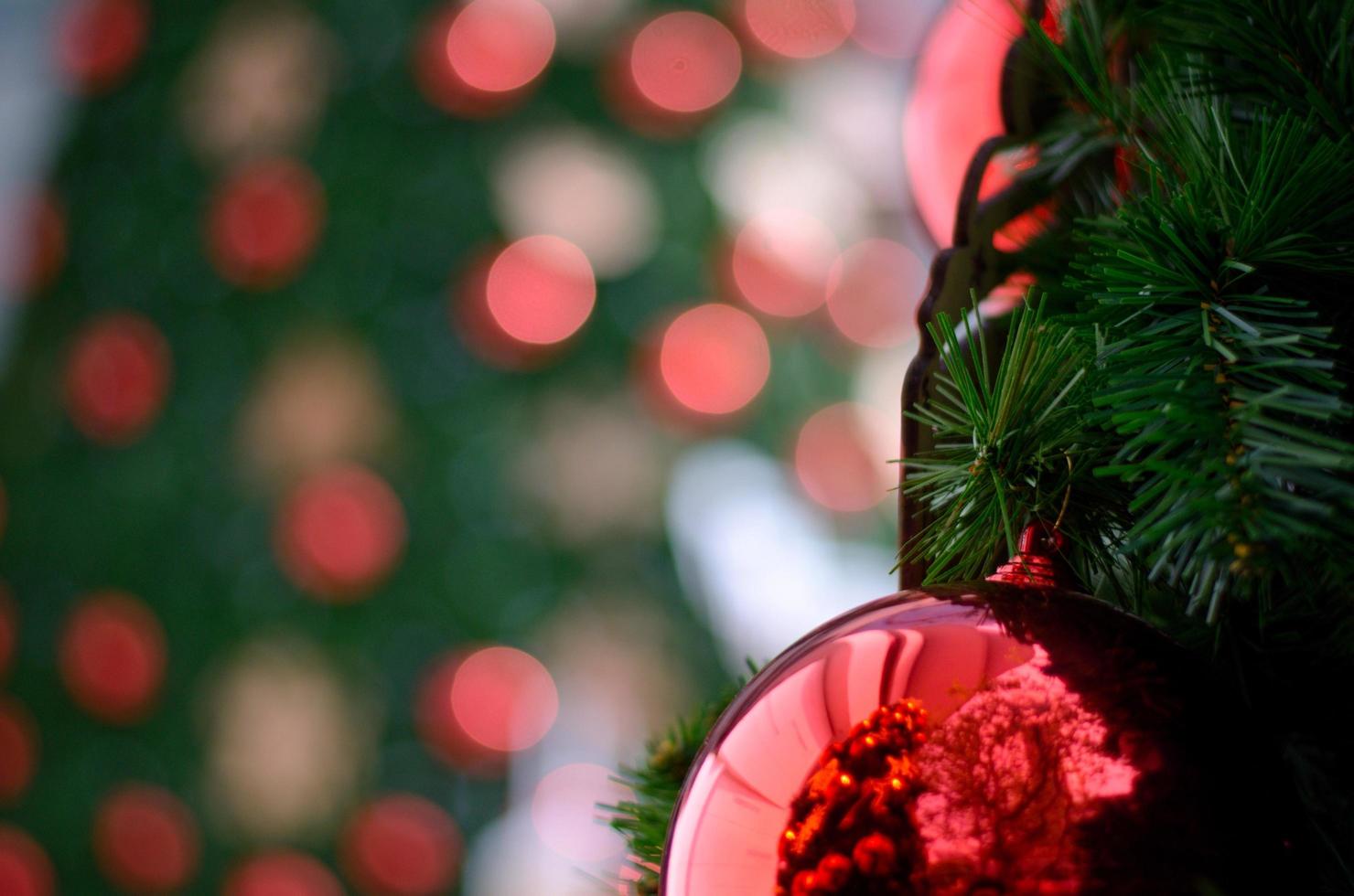 bugiganga vermelha e luzes decoram na árvore de natal com fundo bokeh de outra árvore de natal. foto