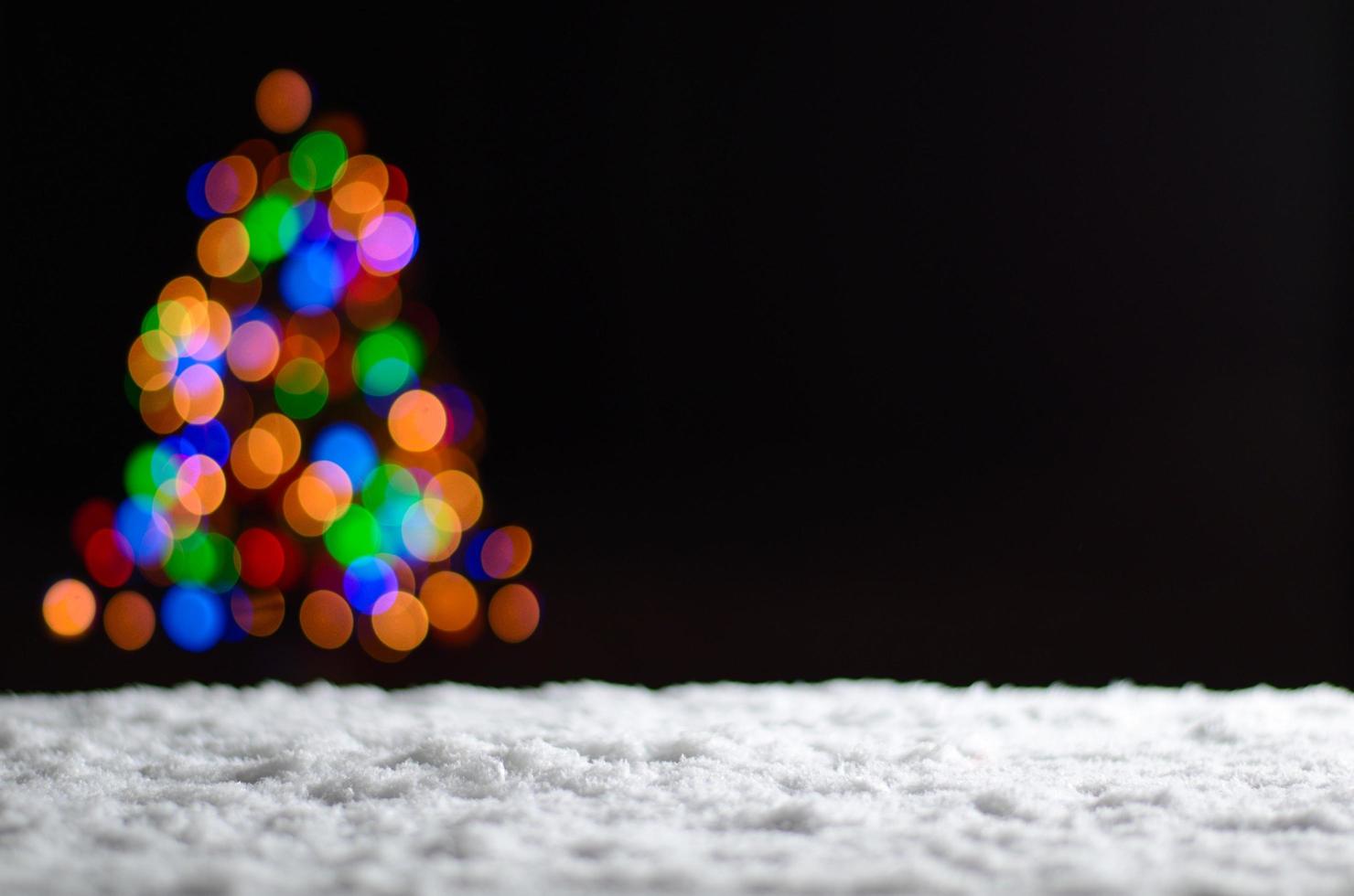 luzes coloridas de bokeh da árvore de natal ao nevar no chão. foto
