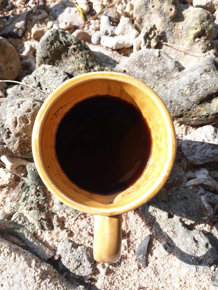 uma xícara de café preto em uma xícara marrom, na areia da praia foto