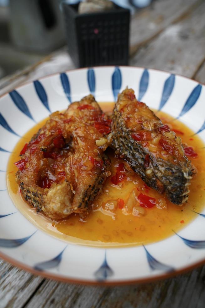 peixe frito com pimenta em um prato de cerâmica sobre um velho piso de madeira. o sabor é azedo, doce e levemente picante. foto