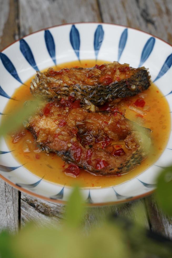 peixe frito com pimenta em um prato de cerâmica sobre um velho piso de madeira. o sabor é azedo, doce e levemente picante. foto