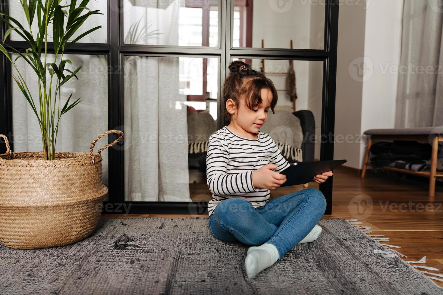 menina com pão com interesse assistindo desenhos em tablet e sentado no chão foto