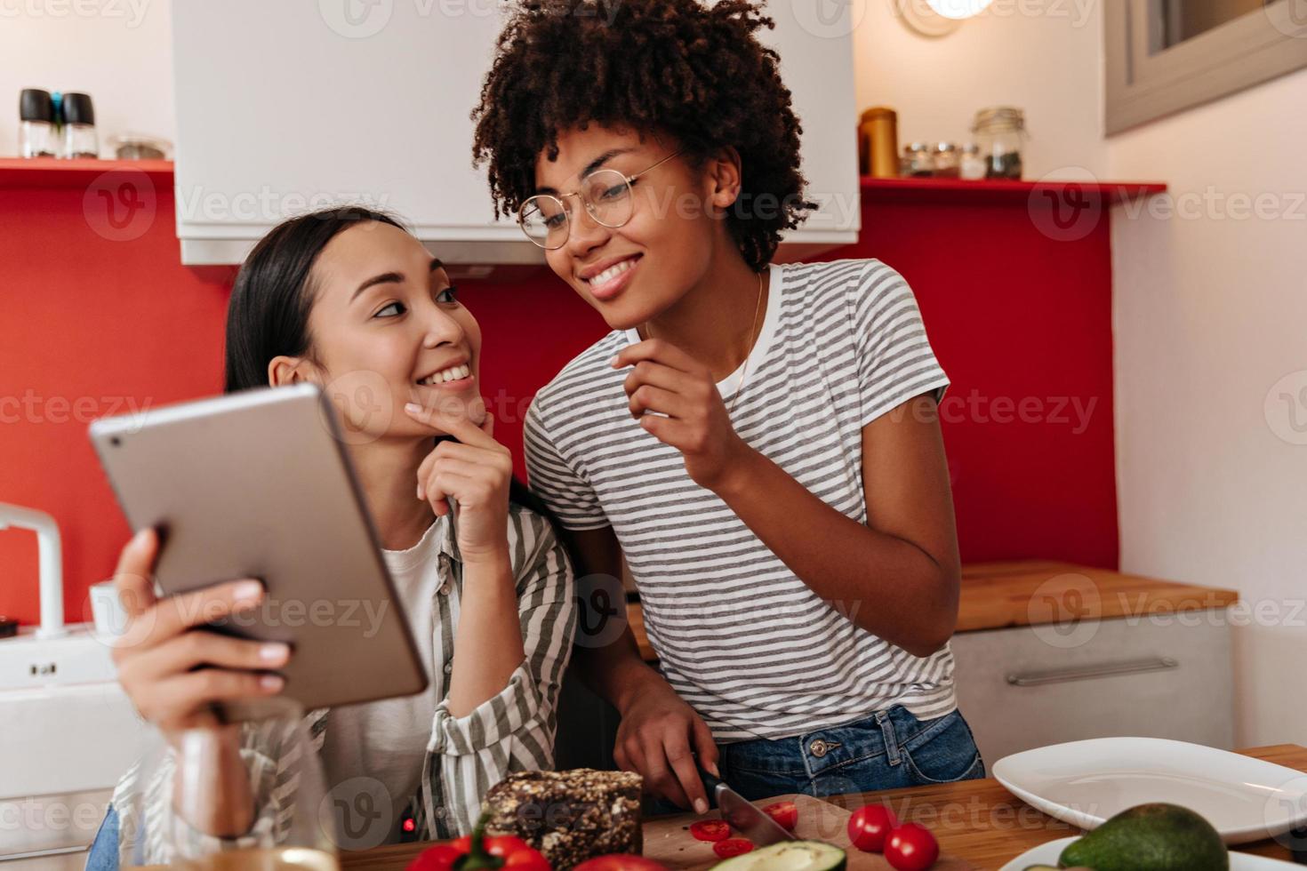 mulheres jovens olham para tablet com interesse enquanto cozinham um almoço saudável. foto