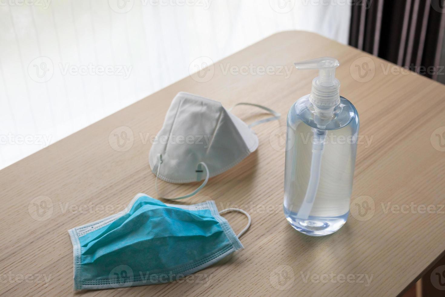 máscara facial médica com gel desinfetante de álcool lavar as mãos na mesa de madeira para o conceito de prevenção de coronavírus covid-19 foto