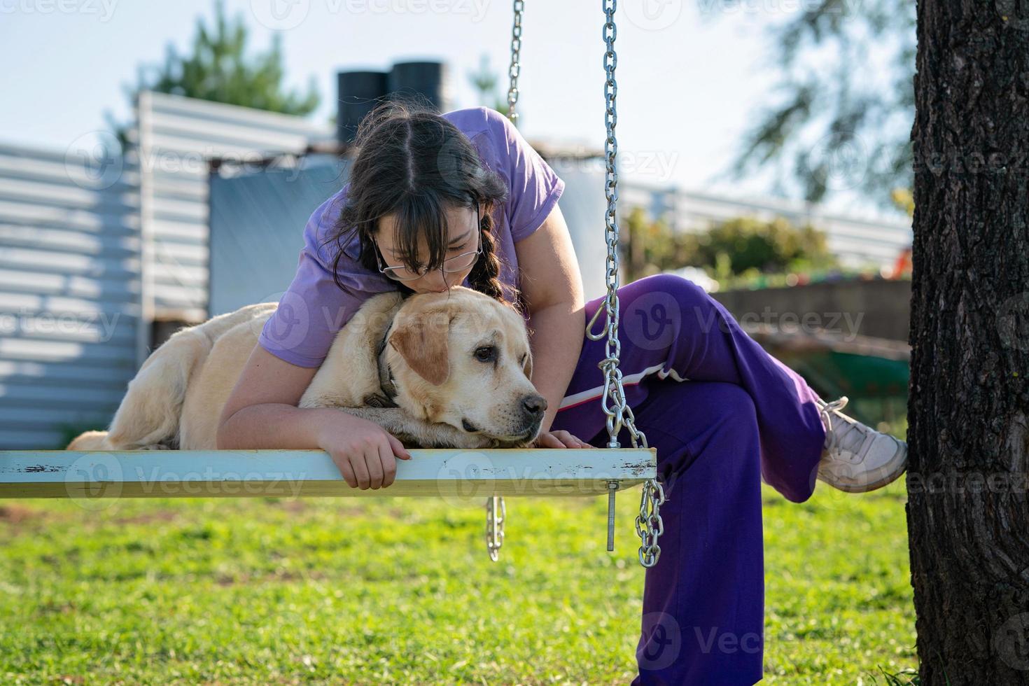 uma adolescente balança em um balanço com seu velho cachorro labrador foto