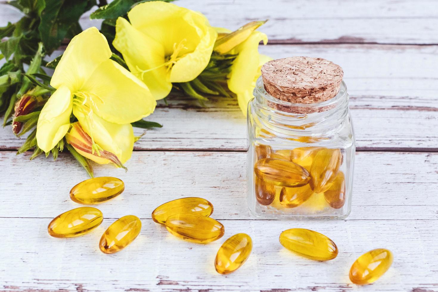 cápsulas de gel de óleo de prímula em frasco de vidro, pílulas e flores amarelas na mesa de madeira foto