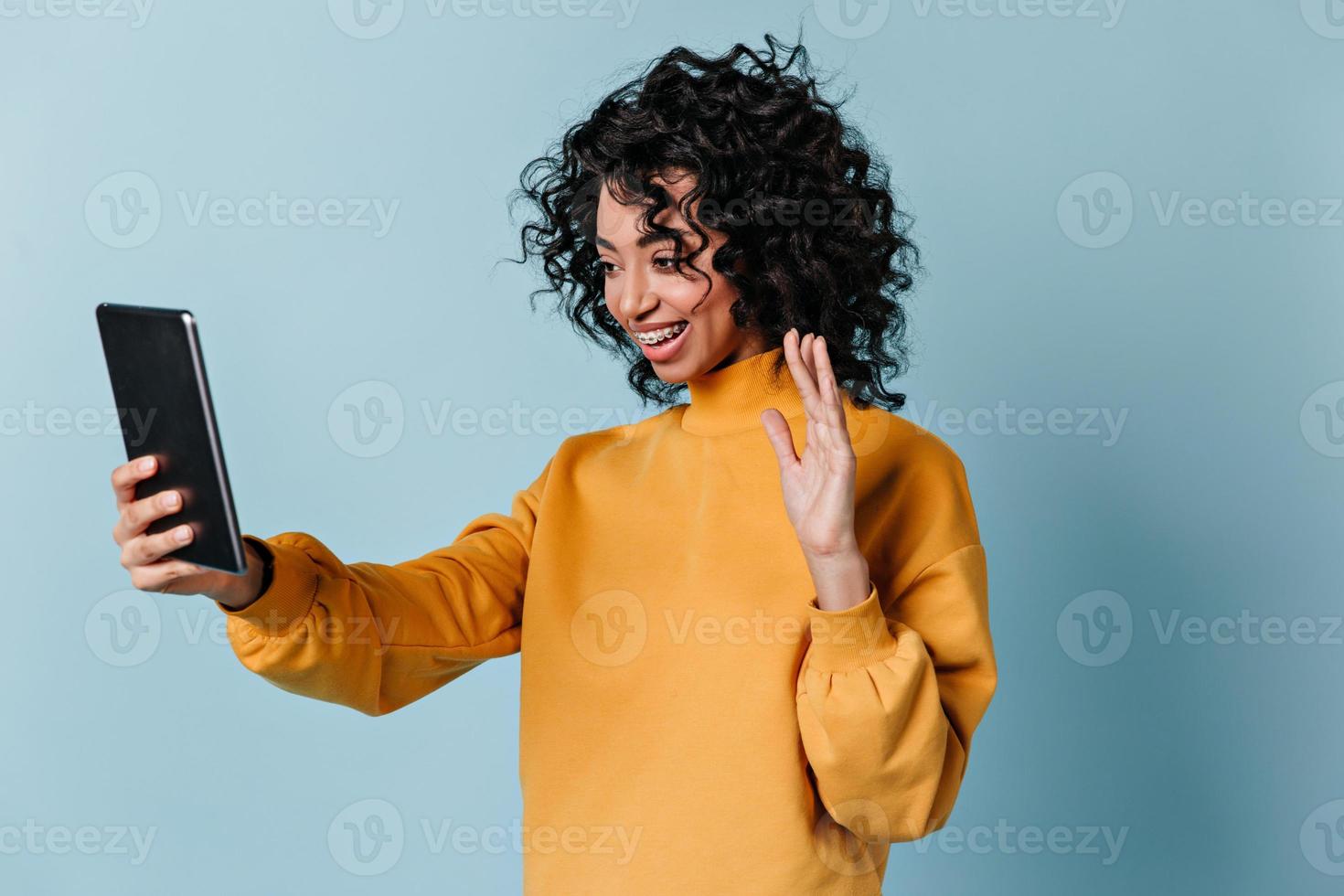 garota em êxtase acenando com a mão durante a chamada de vídeo. mulher de raça mista feliz usando tablet digital. foto