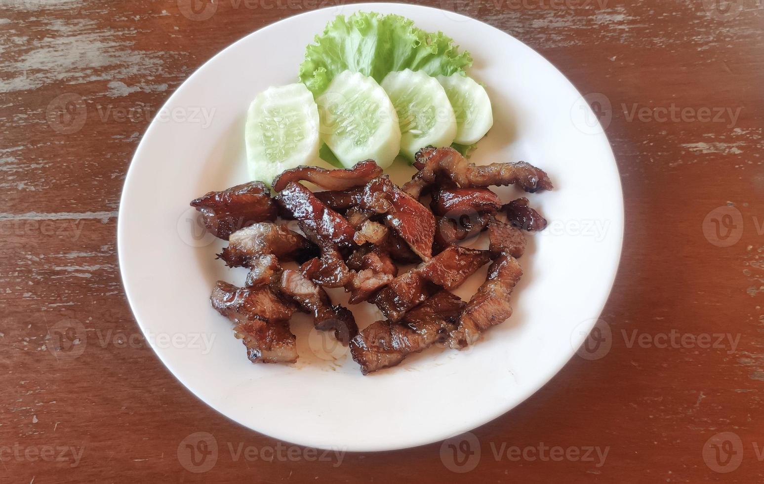 pescoço de porco de churrasco marinado grelhado com molho temperado na chapa branca com pepino ao lado. conceito de comida de rua tailandesa asiática. foto