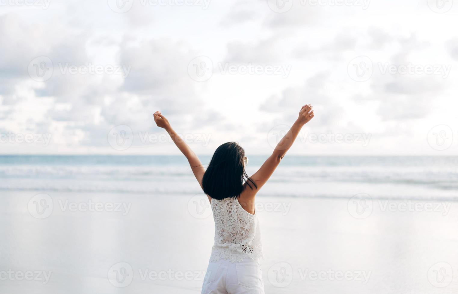 vista traseira da jovem mulher asiática adulta esticando a mão e o braço aberto relaxe na praia. foto
