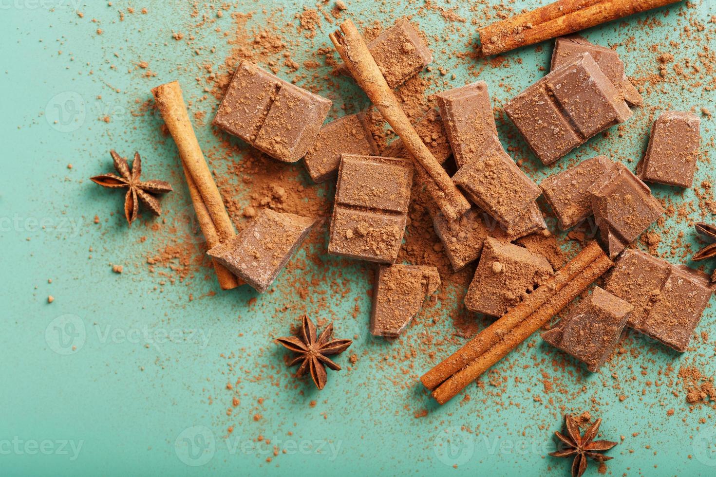 chocolate partido em fatias com cacau em pó e especiarias sobre fundo verde foto