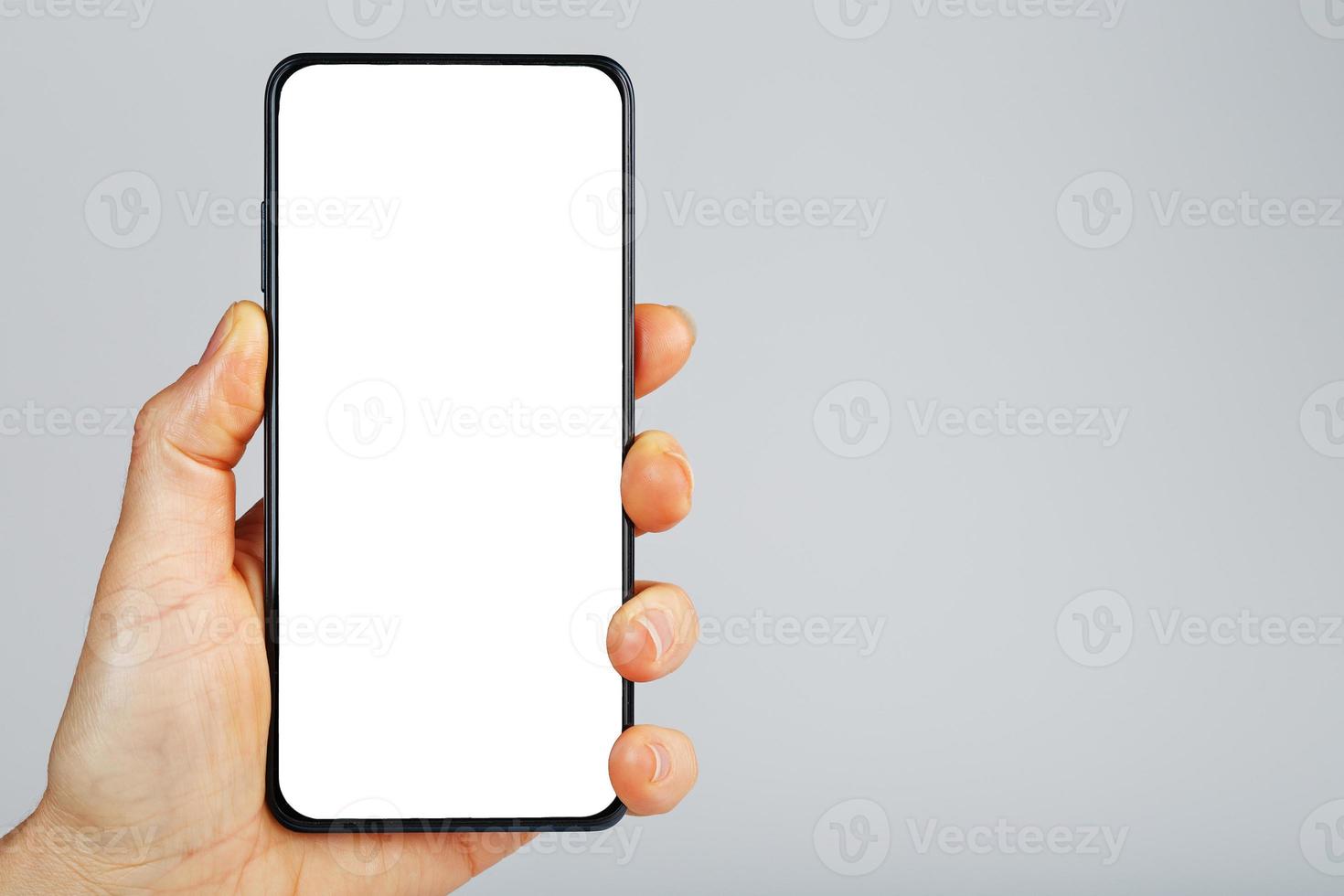 mão segura smartphone preto com tela branca em branco e design moderno sem moldura isolado em fundo cinza. foto