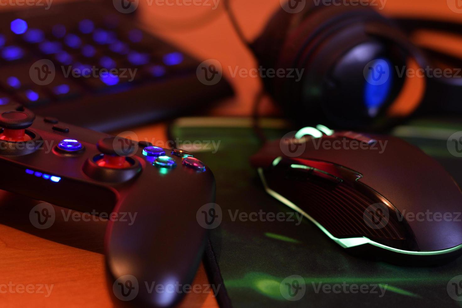 gamepad moderno e mouse para jogos encontra-se com teclado e fones de ouvido na mesa na cena da sala de jogos escura. conceito de jogo em equipe cooperativo foto