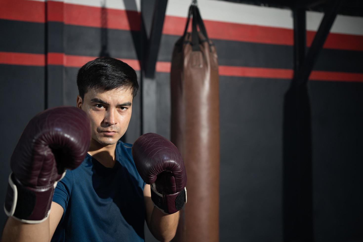 boxer de homens caucasianos bonitos sem camisa com soco de boxe de treinamento muscular forte no lado do ginásio com saco de areia. atividade de treino cardio esporte para uma boa saúde e construir corpo e força física. foto