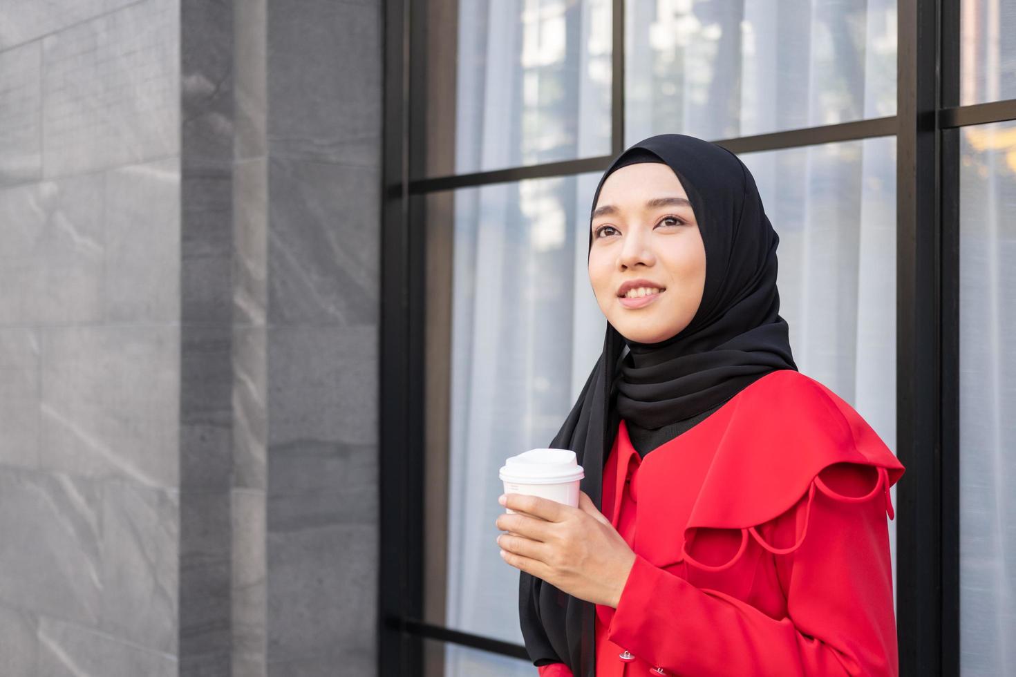 belas mulheres islâmicas do leste asiático usando hijab com vestido formal. segurando a xícara de café e andando na área urbana da cidade, sentindo-se feliz e sorrindo. conceito de estilo de vida de pessoas com espaço de cópia. foto