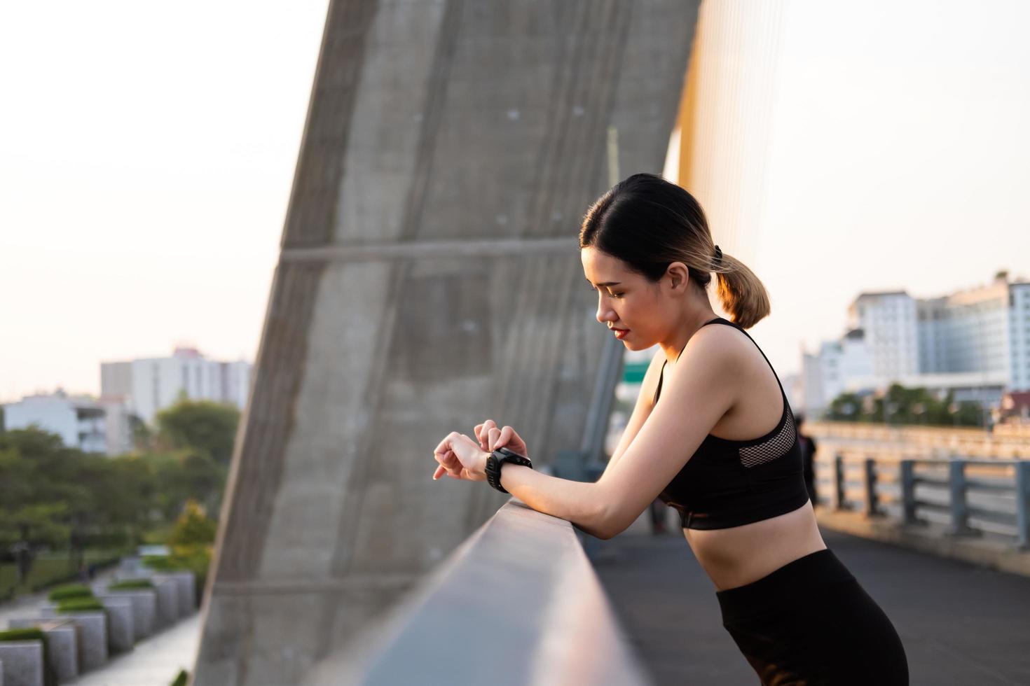 foco seletivo no rosto de jovens mulheres asiáticas bonitas usando relógio inteligente para rastrear a atividade e ouvir música enquanto se aquece antes do exercício ou correndo na vista da cidade urbana. estilo de vida em forma e saudável. foto