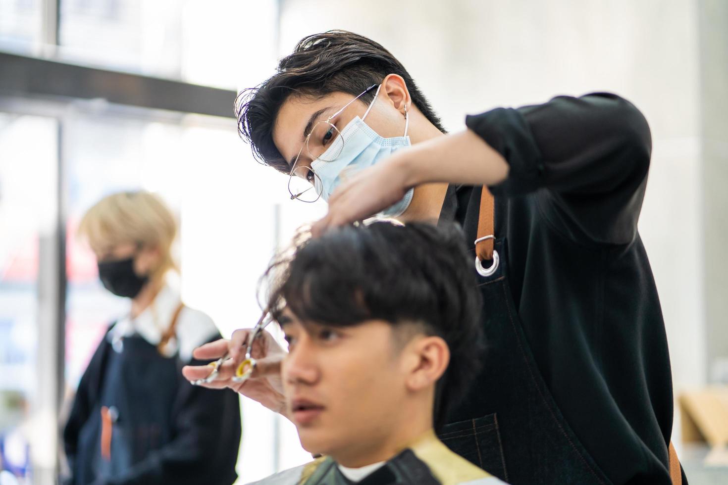 homens asiáticos têm estilo com o cliente enquanto cortam o cabelo e usam máscara cirúrgica enquanto penteiam o cabelo para o cliente. ocupação profissional, serviço de beleza e moda novo normal foto