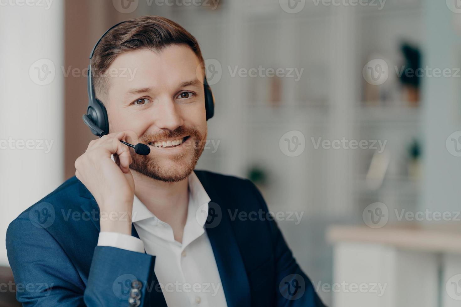 feliz jovem empresário usando fones de ouvido com microfone falando com clientes dentro de casa foto