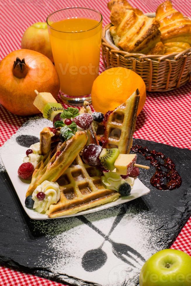 closeup vertical de deliciosa sobremesa, waffles com frutas, croissants, suco de laranja, servido no quadro negro foto
