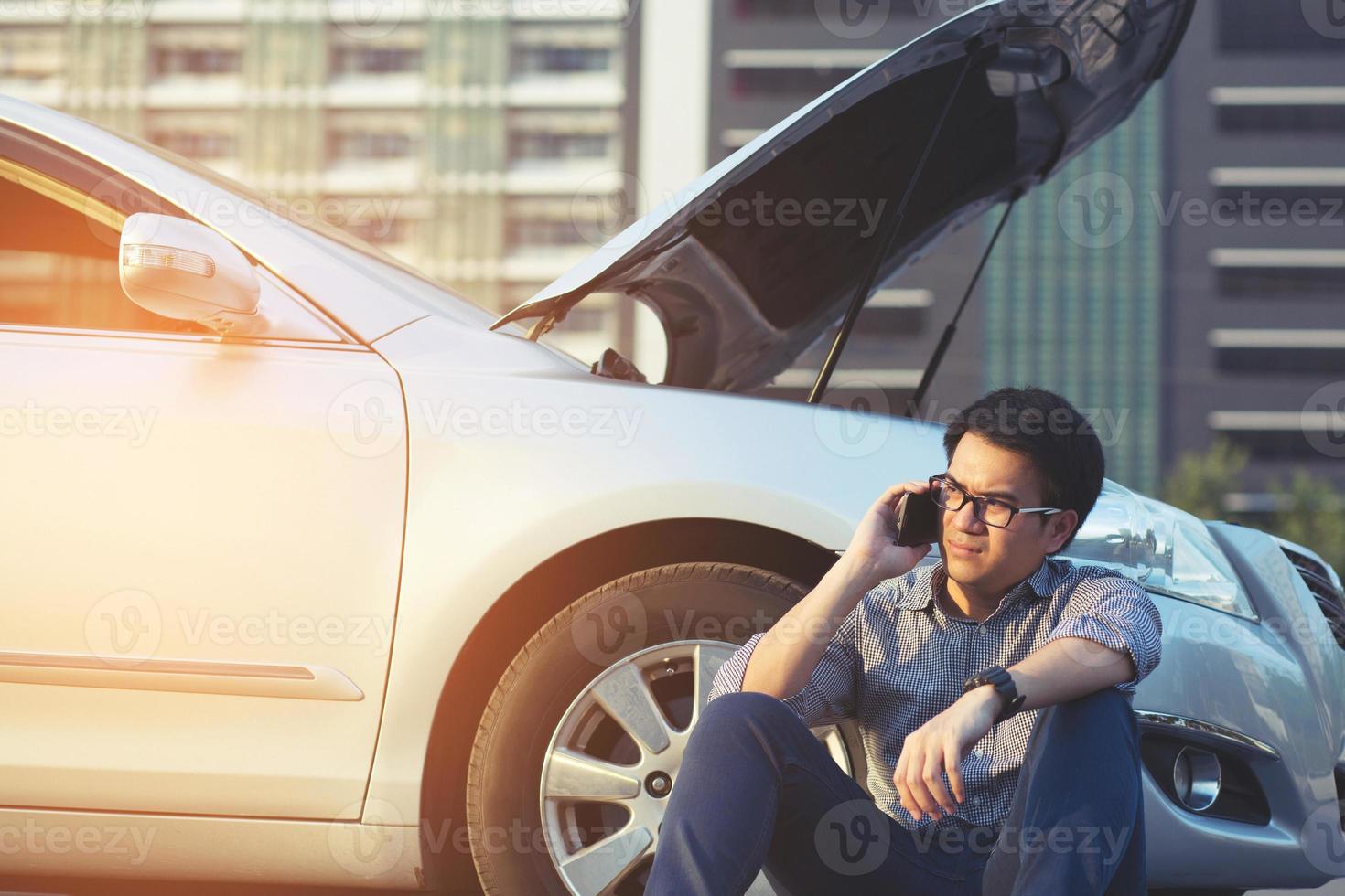 homem irritado sente-se na frente de um carro quebrado pedindo ajuda foto