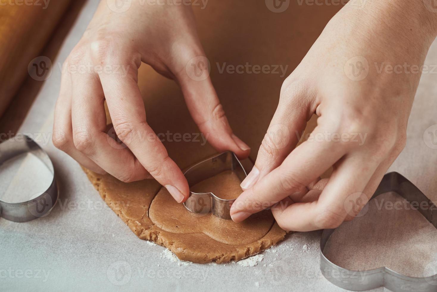 fazendo biscoitos de gengibre em forma de coração para o dia dos namorados. mão de mulher usa cortador de biscoitos. conceito de comida de férias foto