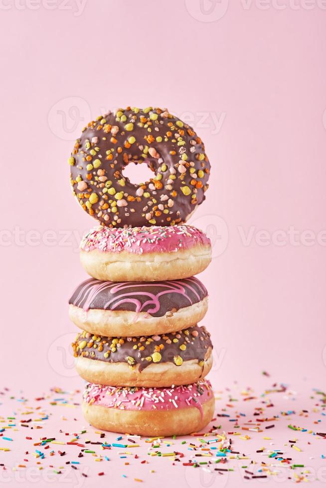 pilha de donuts coloridos decorados em um fundo rosa foto