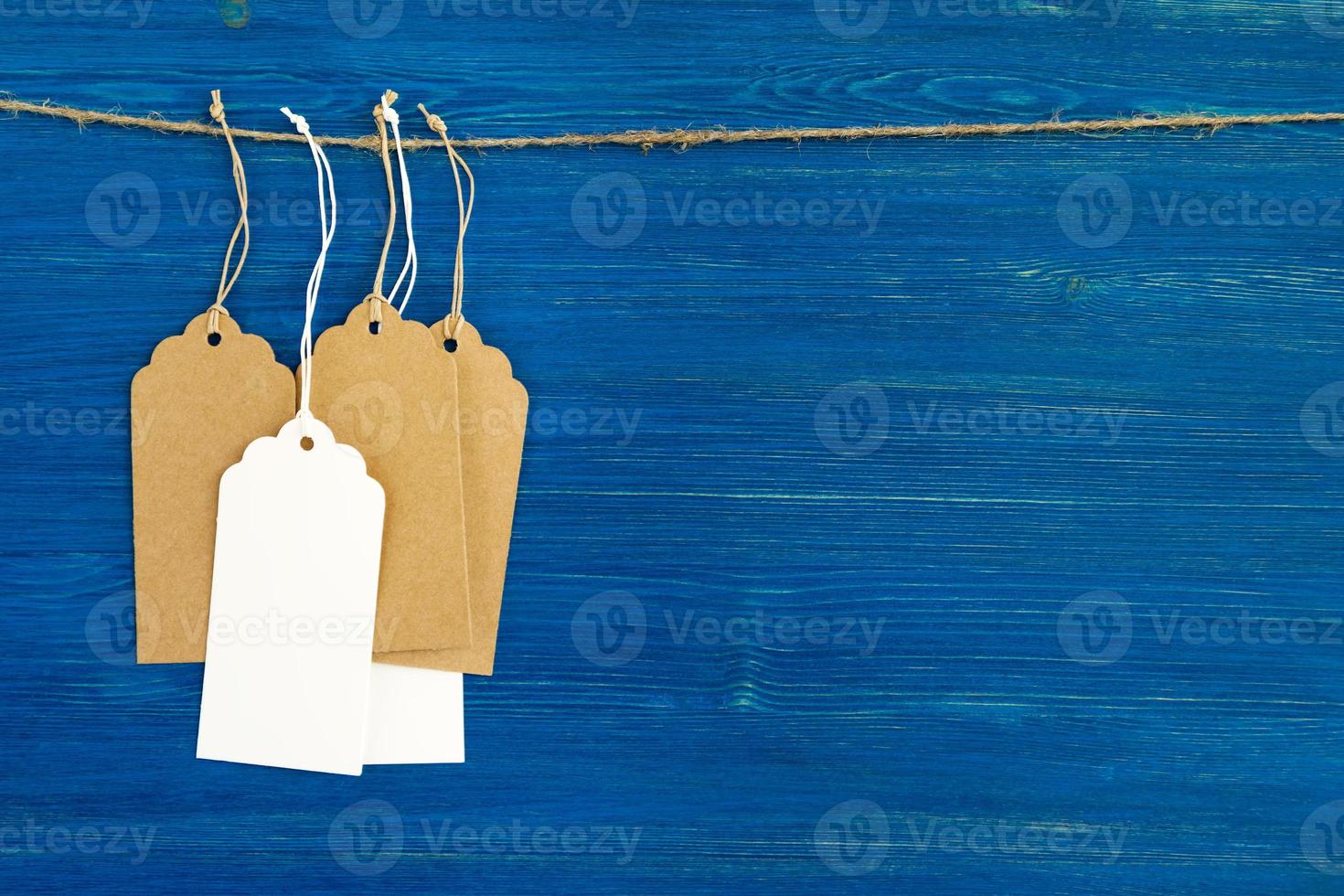etiquetas de preço de papel em branco marrom e branco ou etiquetas penduradas em uma corda sobre o fundo azul de madeira. foto