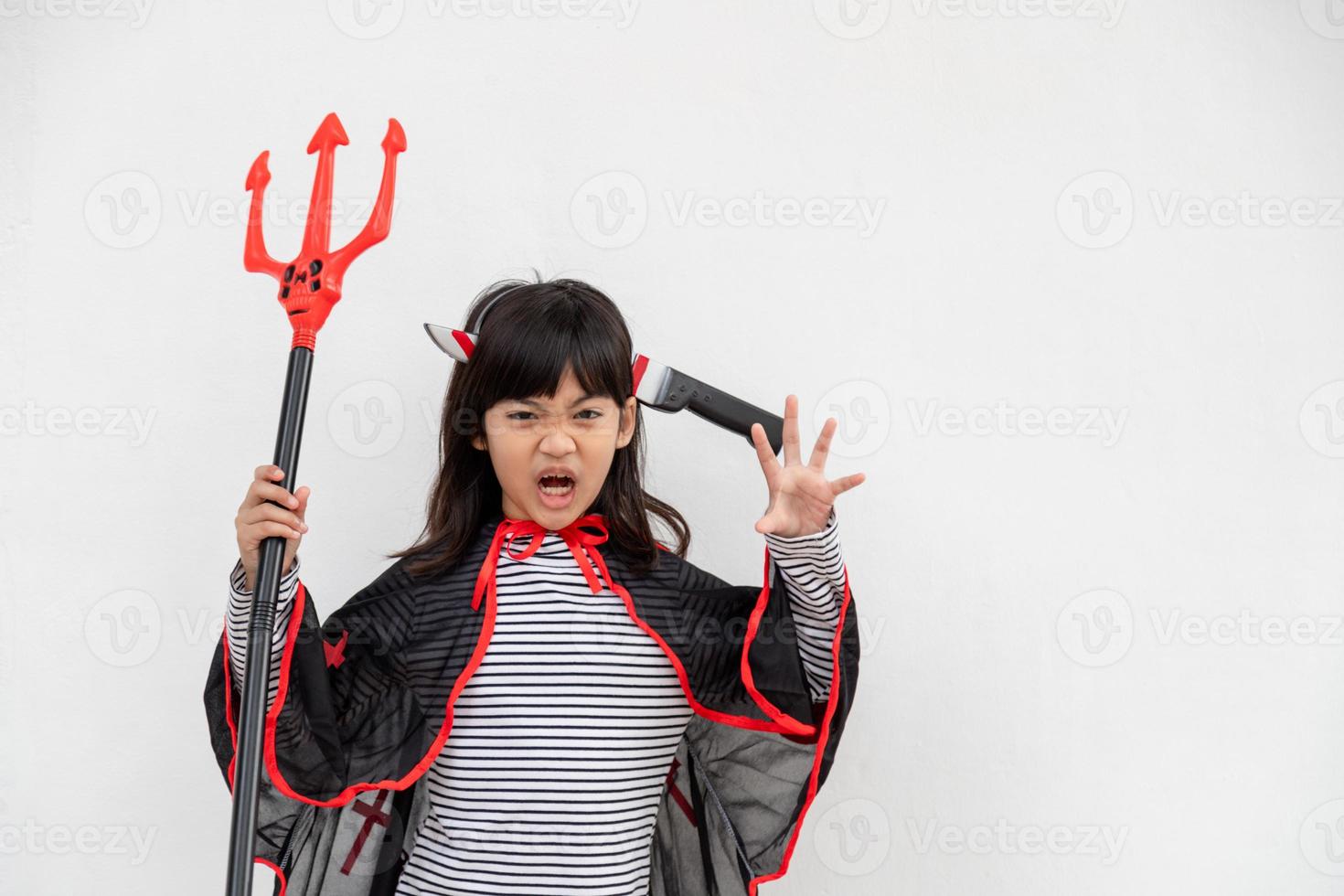 menina criança asiática em fantasia de demônio segurando tridente preto e vermelho, conceito de feliz dia das bruxas foto