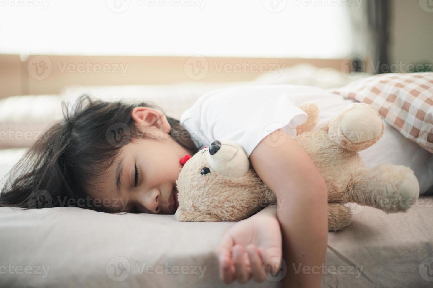 criança menina dorme na cama com um ursinho de pelúcia de brinquedo foto