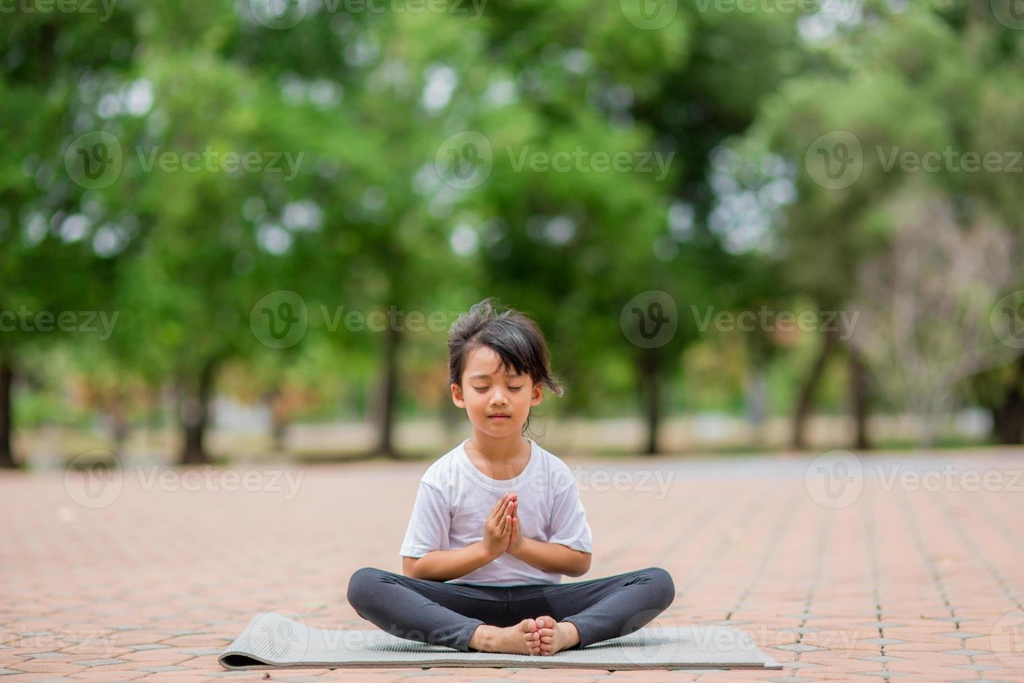 menina asiática bonitinha praticando pose de ioga em um tapete no parque, conceito saudável e exercício foto