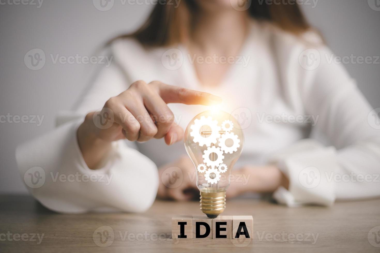 mão tocando na lâmpada no bloco de madeira com ideia de palavra, novo conceito de ideia com inovação e inspiração, tecnologia inovadora no conceito de ciência e comunicação. foto