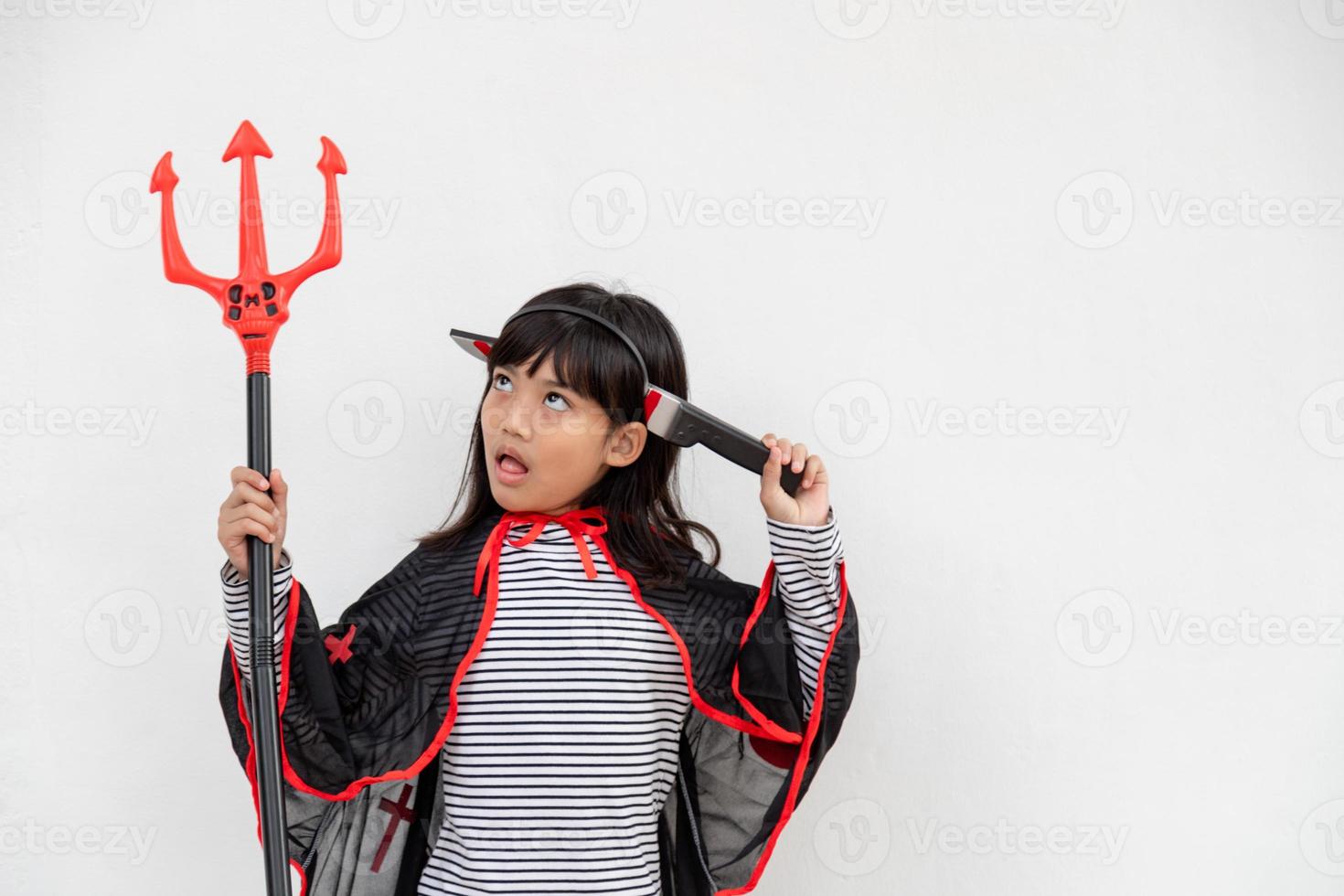 menina criança asiática em fantasia de demônio segurando tridente preto e vermelho, conceito de feliz dia das bruxas foto