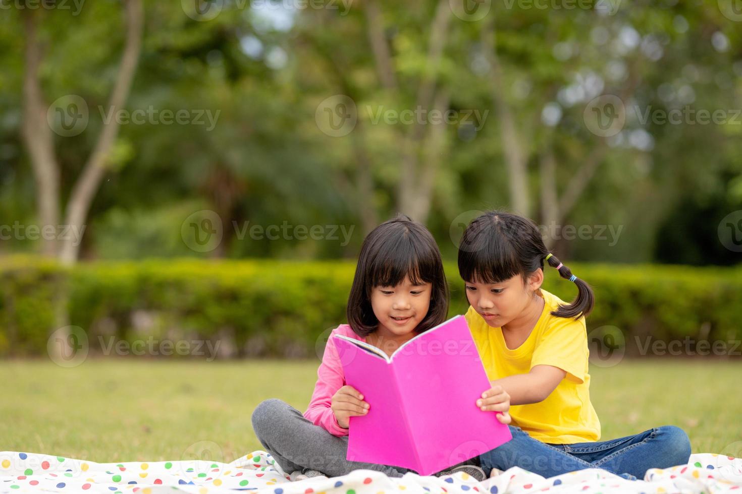 duas lindas meninas lendo livros no jardim, sentado na grama. o conceito de educação e amizade. foto