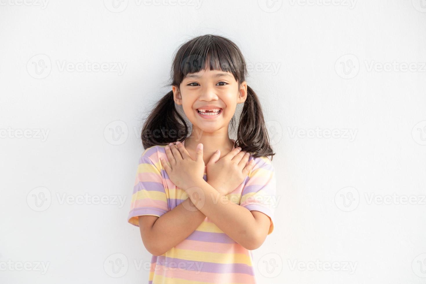 close-up de linda menina feliz isolada no fundo branco de mãos dadas no peito do coração sinta-se grato, sorrindo criança com os olhos fechados orar agradecendo a Deus altos poderes, conceito de fé foto