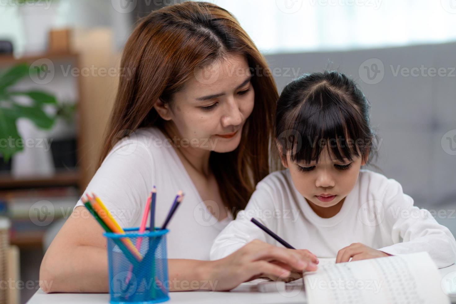 linda mulher asiática ajudando a filha com a lição de casa em casa. foto