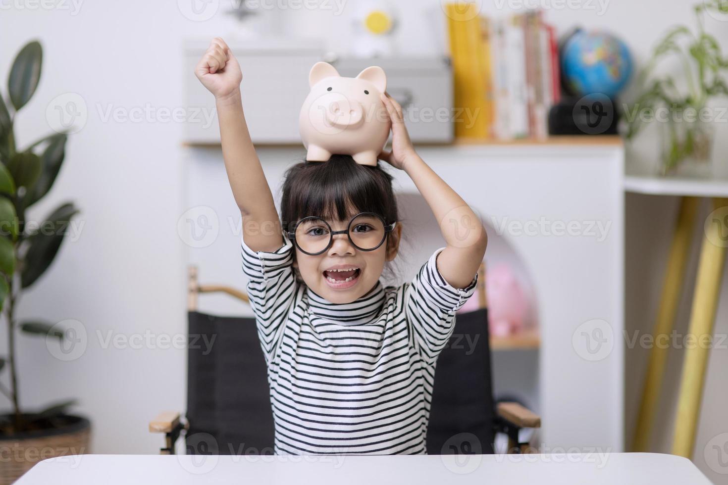 menina asiática economizando dinheiro em um cofrinho, aprendendo sobre economia, criança economizando dinheiro para educação futura. conceito de dinheiro, finanças, seguro e pessoas foto