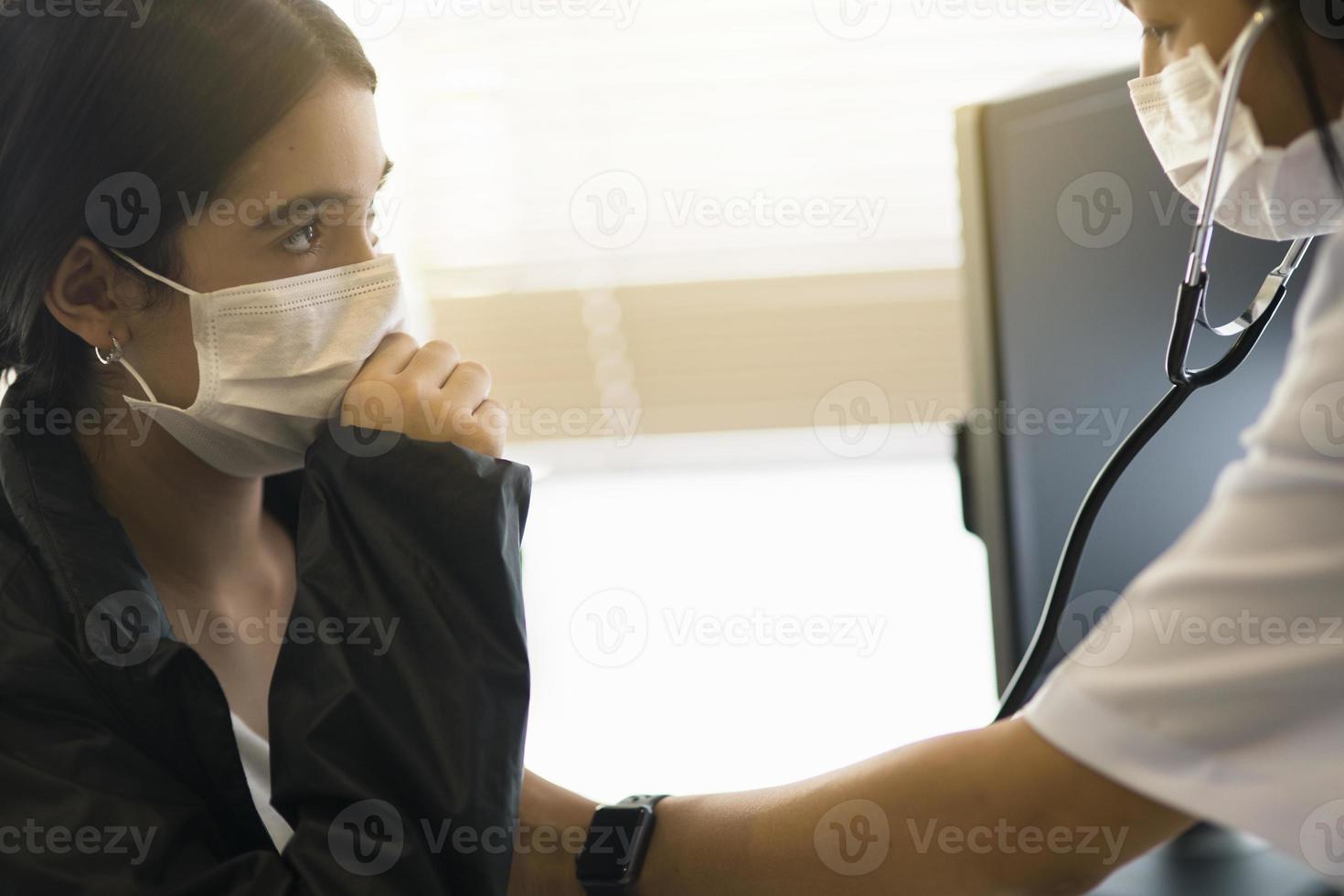 uma médica asiática usando uma máscara cirúrgica está verificando a frequência cardíaca do paciente infantil com um estetoscópio. foto