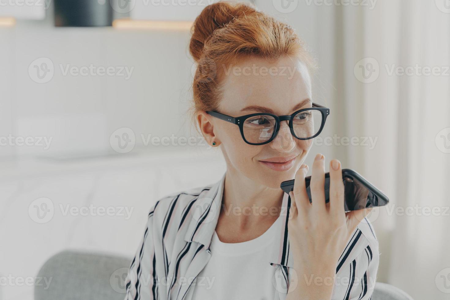 tiro horizontal de mulher ruiva usa assistente de voz no smartphone faz chamada de voz foto