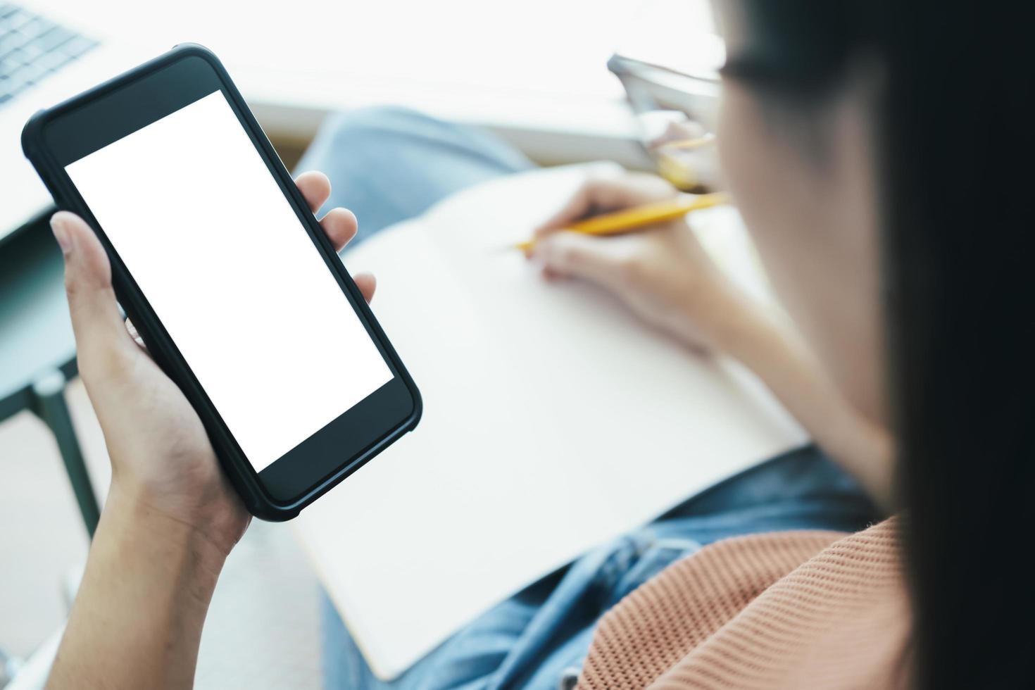 Feche a mão de uma mulher segurando um telefone inteligente e escrevendo um livro foto