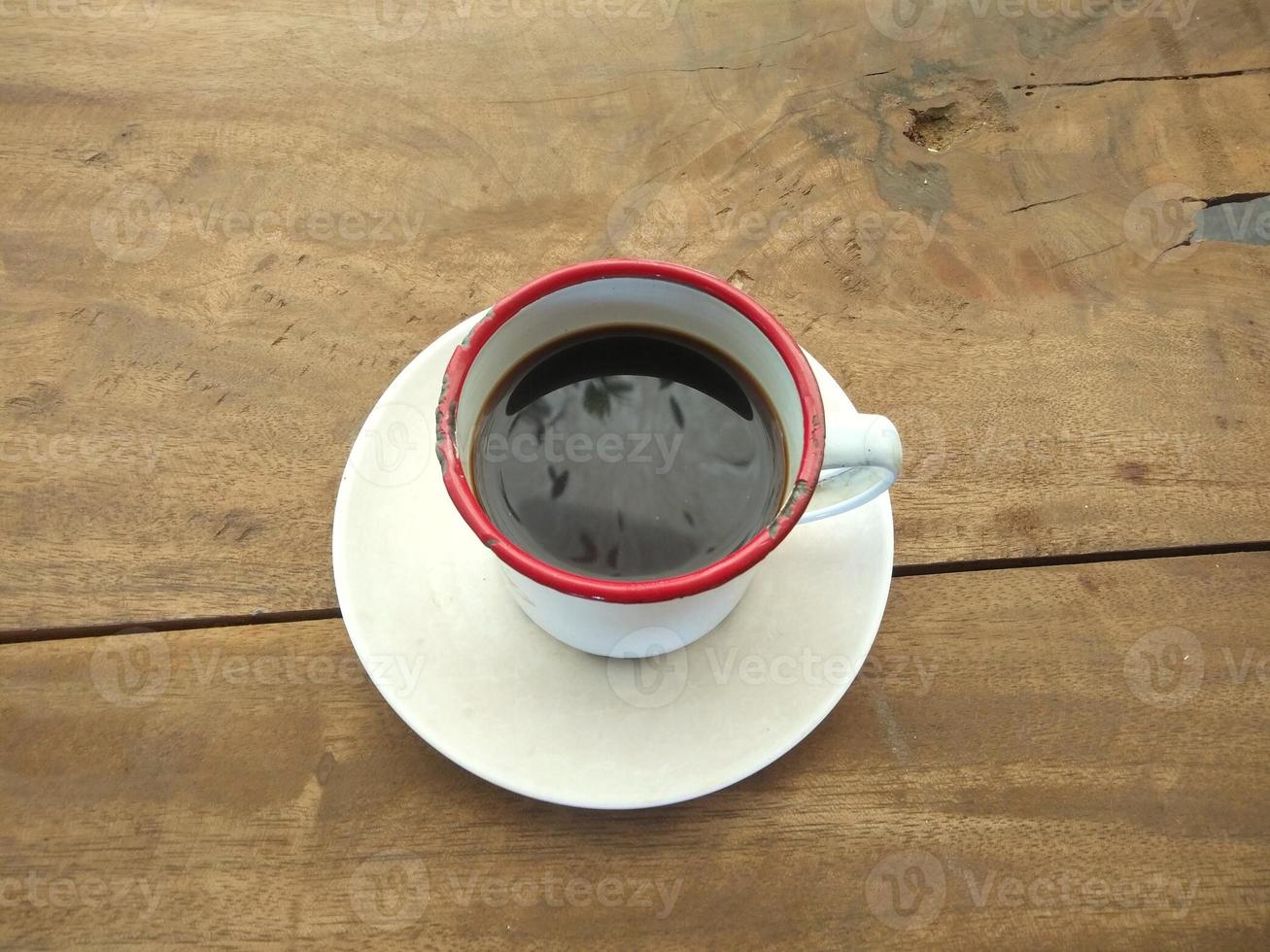 uma xícara de café preto sentado em uma mesa feita de tábuas de madeira foto