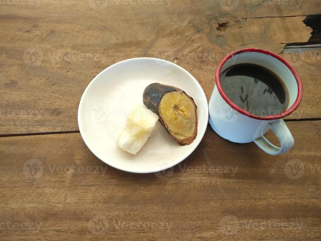 uma xícara de café preto, mandioca cozida e banana cozida em uma mesa feita de tábuas de madeira foto