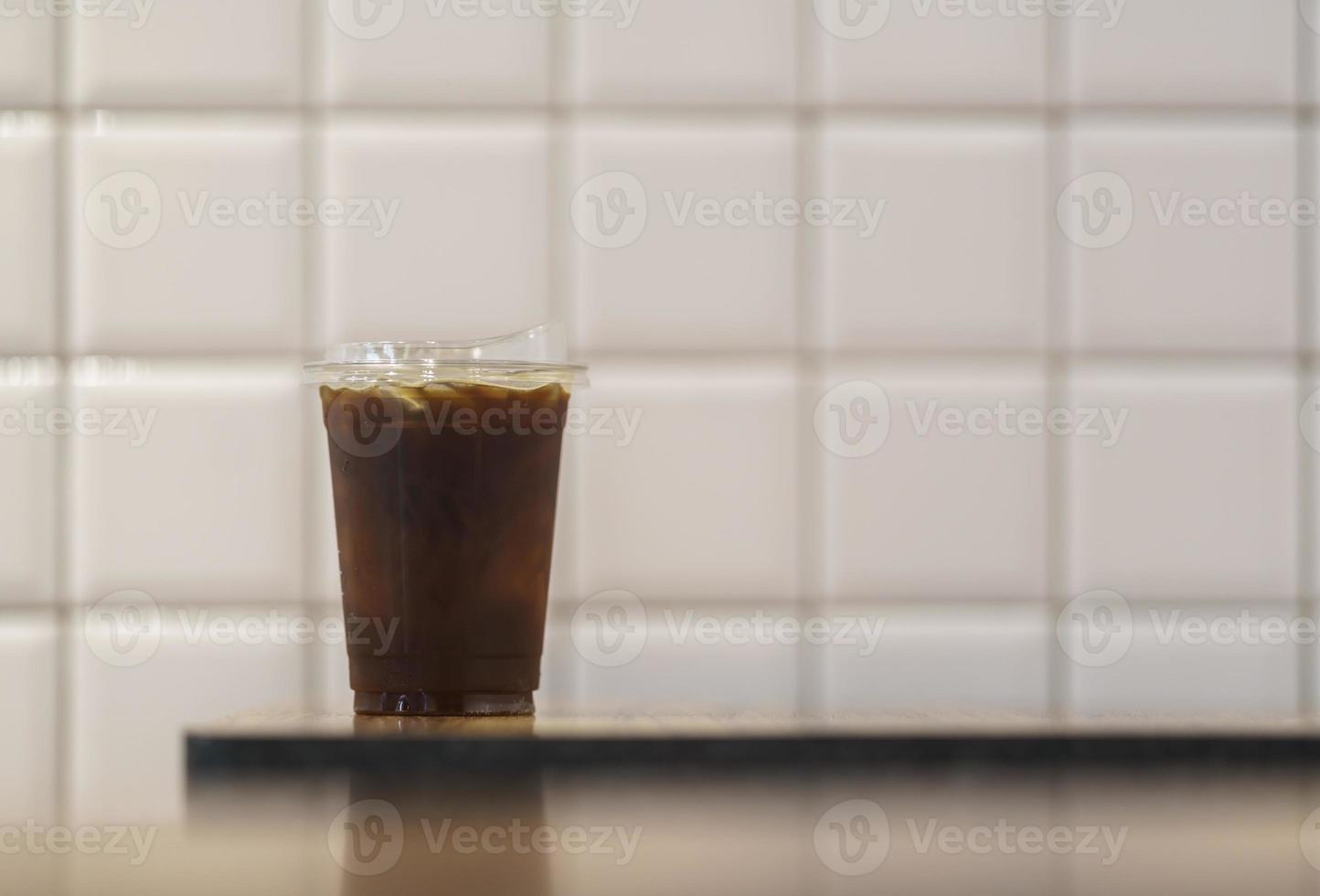 closeup de copo de plástico para viagem de café preto gelado americano na mesa de madeira no restaurante. foto