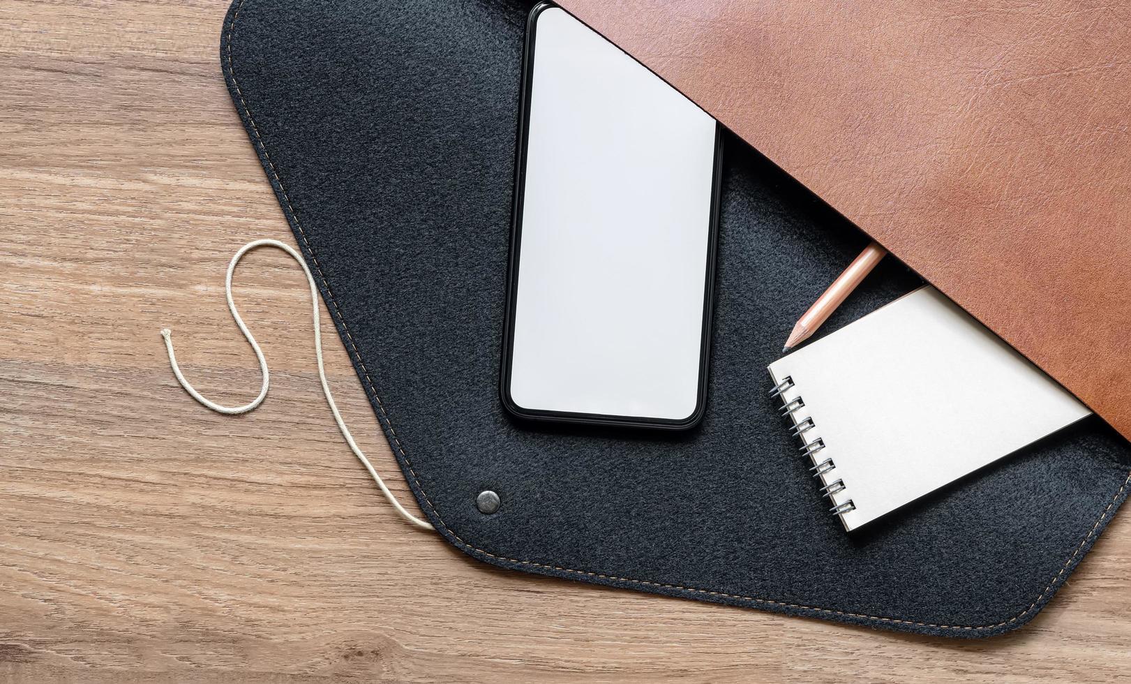 maquete de smartphone com bloco de notas e lápis em uma bolsa de couro foto