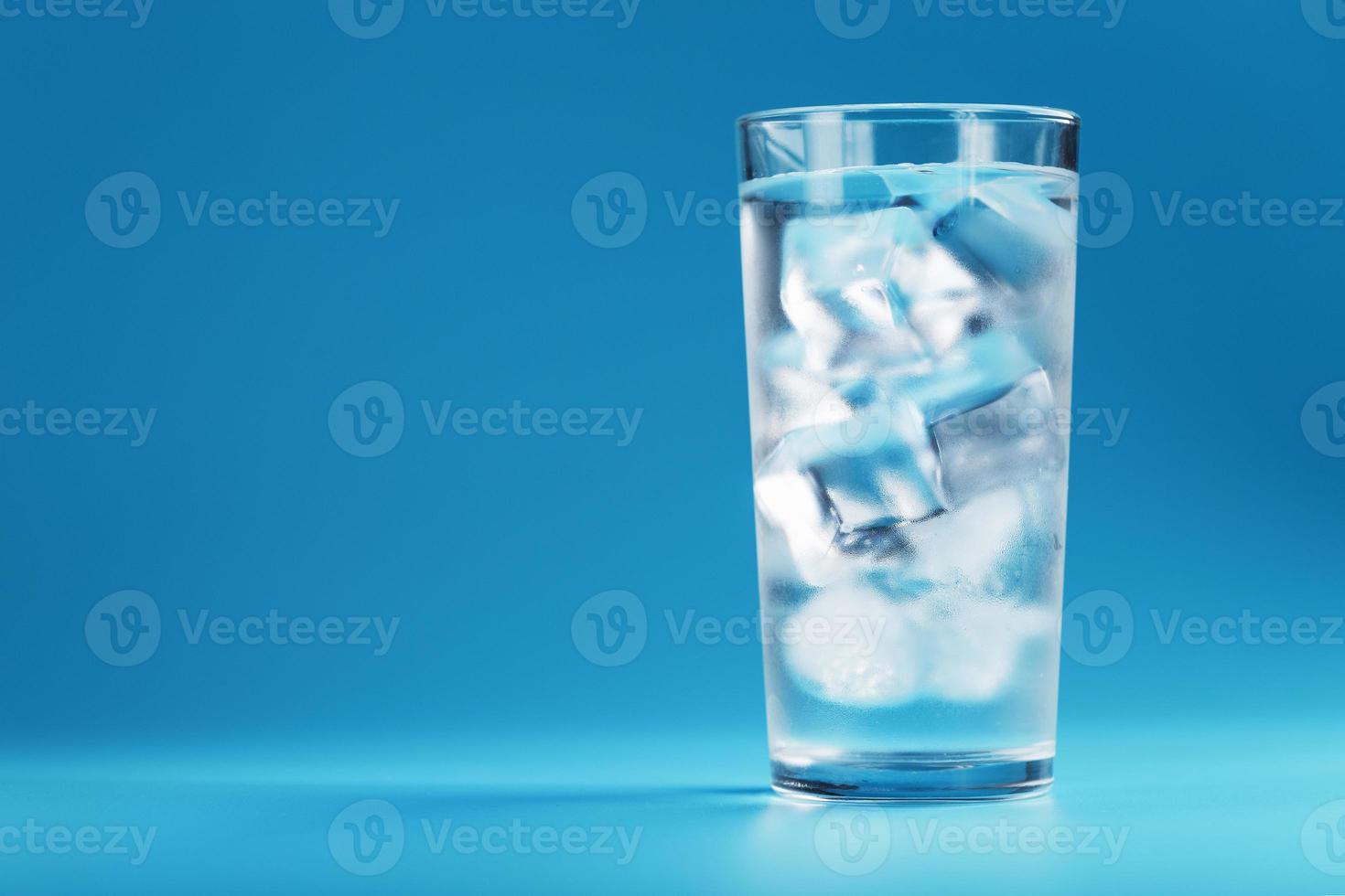 cubos de gelo em um copo com água cristalina em um fundo azul. foto