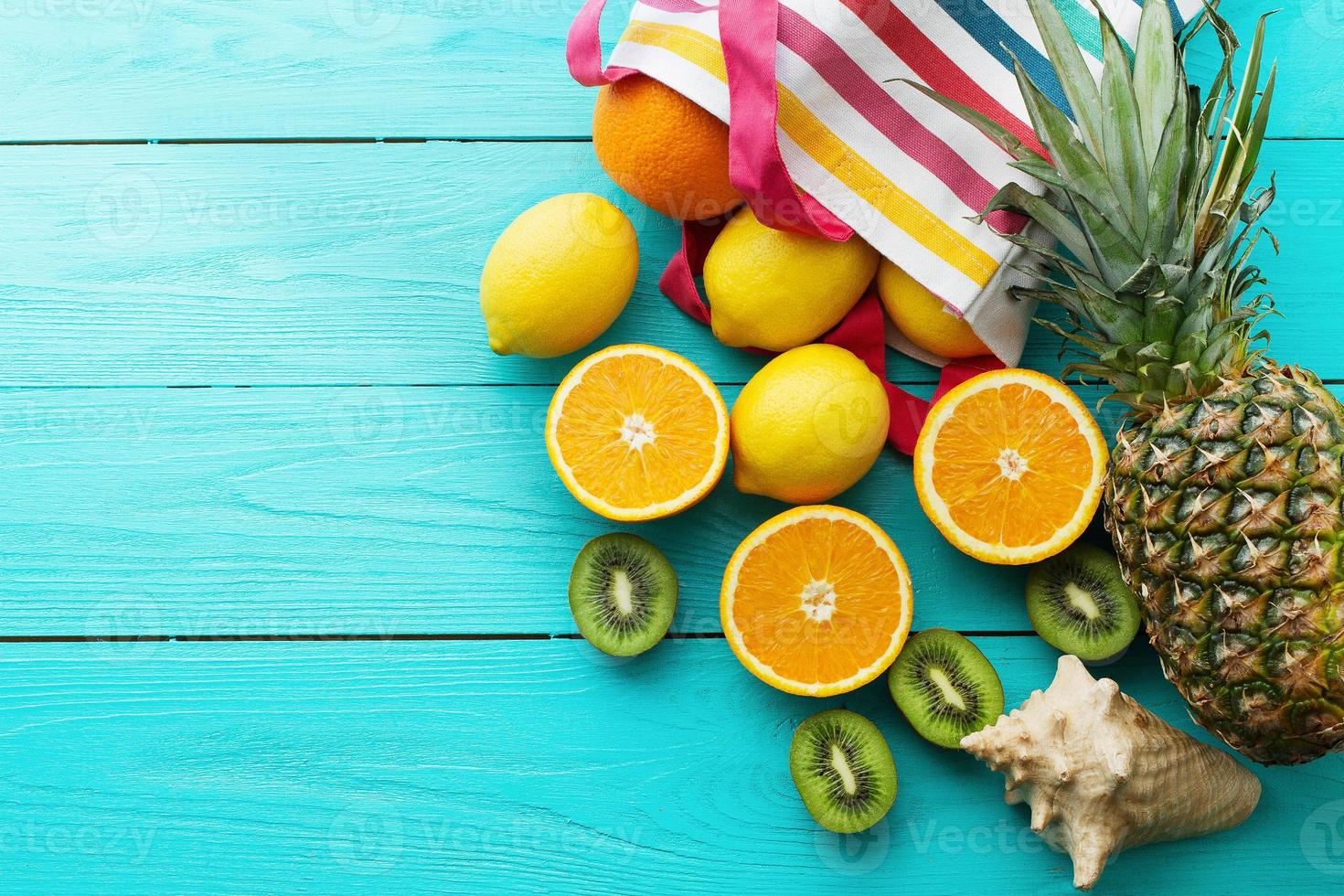 alimentos frescos cítricos. férias de verão. laranja, kiwi, abacaxi, limão e concha do mar sobre fundo azul de madeira. férias e vista summertime.top e copie o espaço. brincar foto