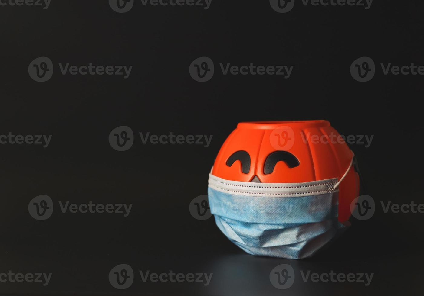 abóbora de halloween de plástico usando máscara facial médica isolada em fundo preto com espaço de cópia. novo conceito normal de halloween foto